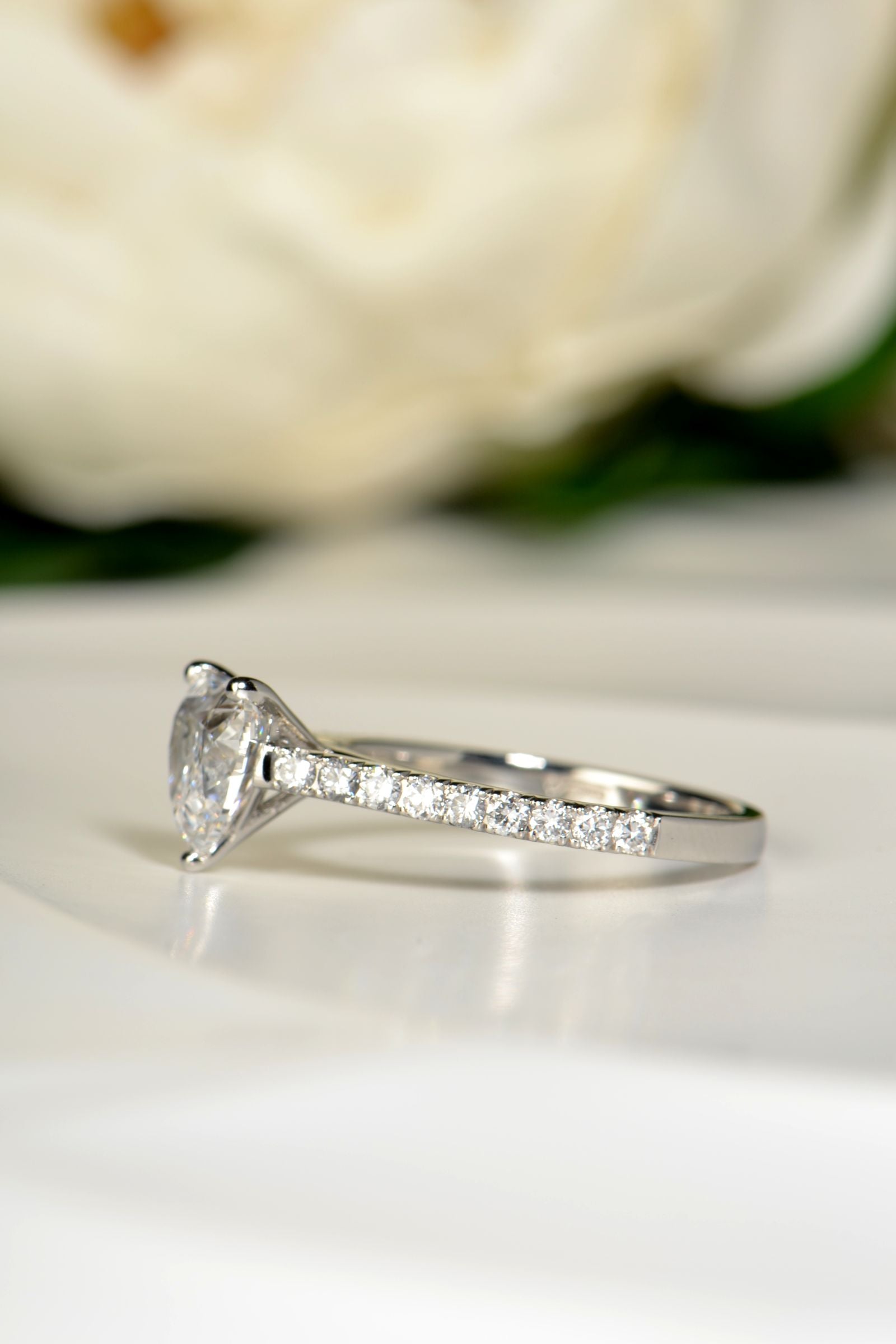Angled view of a platinum heart shaped lab diamond engagement ring, highlighting the hand-set lab diamond shoulders and elegant ribbon-style band.