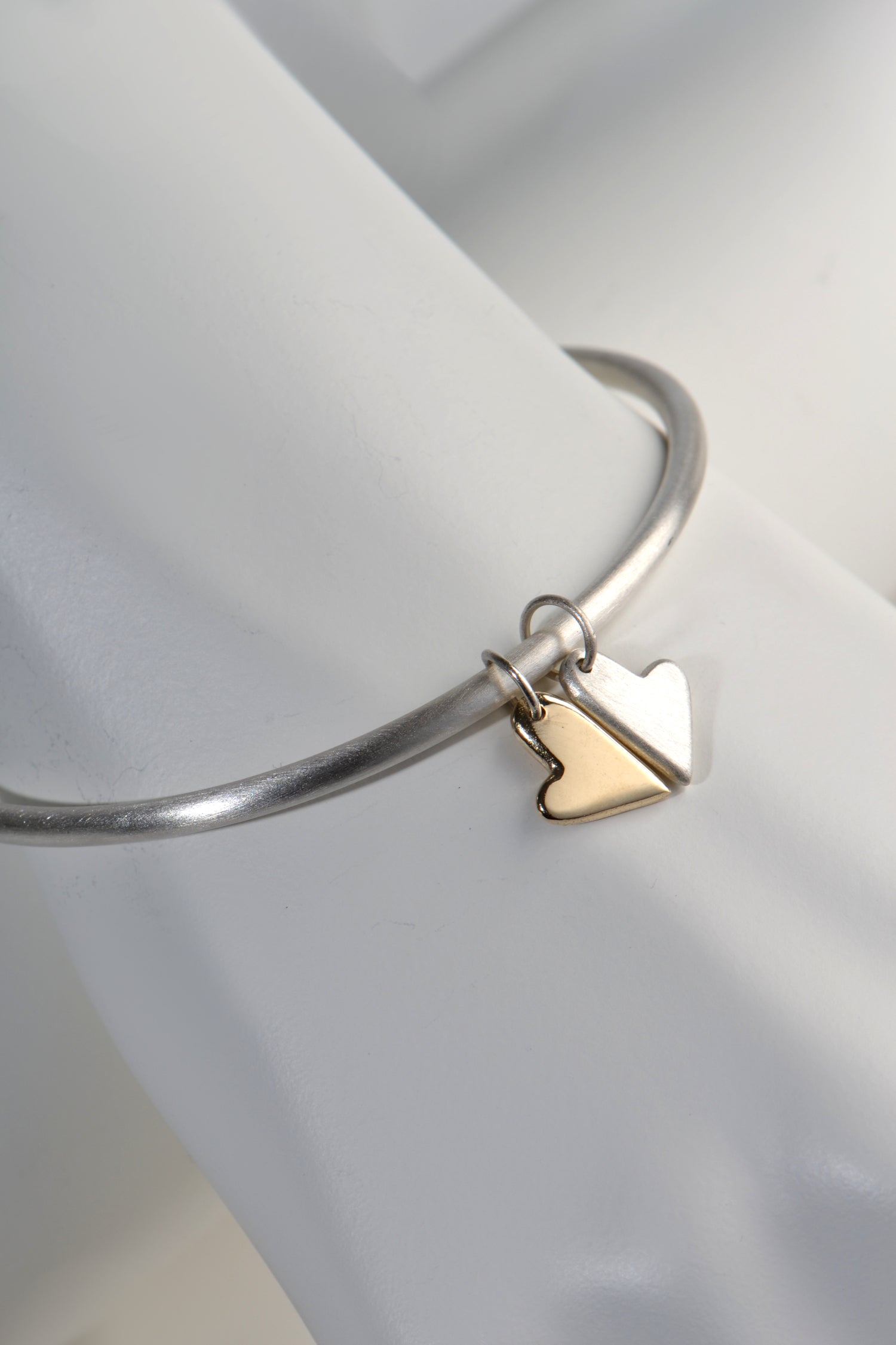 silver handmade bangle with two moving heart charms, one in silver and one in gold