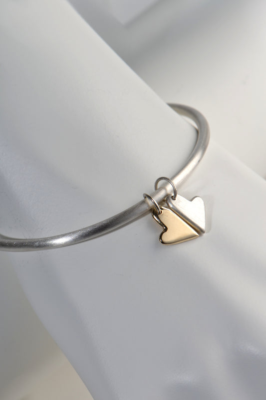 silver handmade bangle with two moving heart charms, one in silver and one in gold