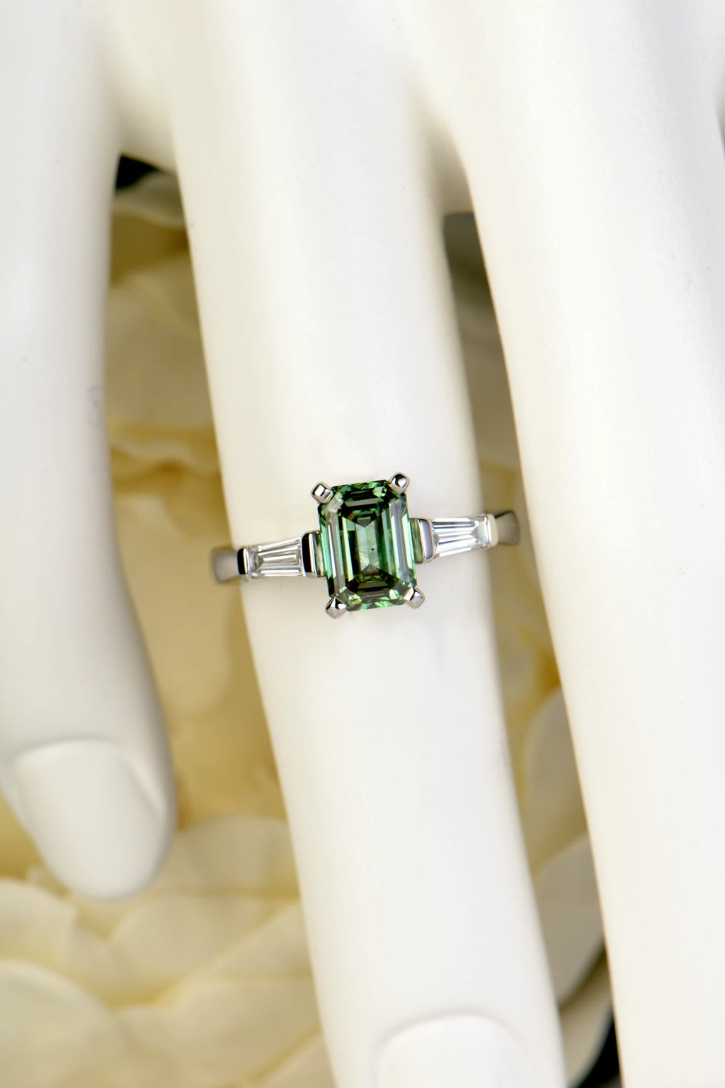 A luxury 950 platinum trilogy ring featuring a 1.50ct emerald-cut vivid green lab-grown diamond and tapered baguettes being worn on a hand model to demonstrate scale and brilliance.