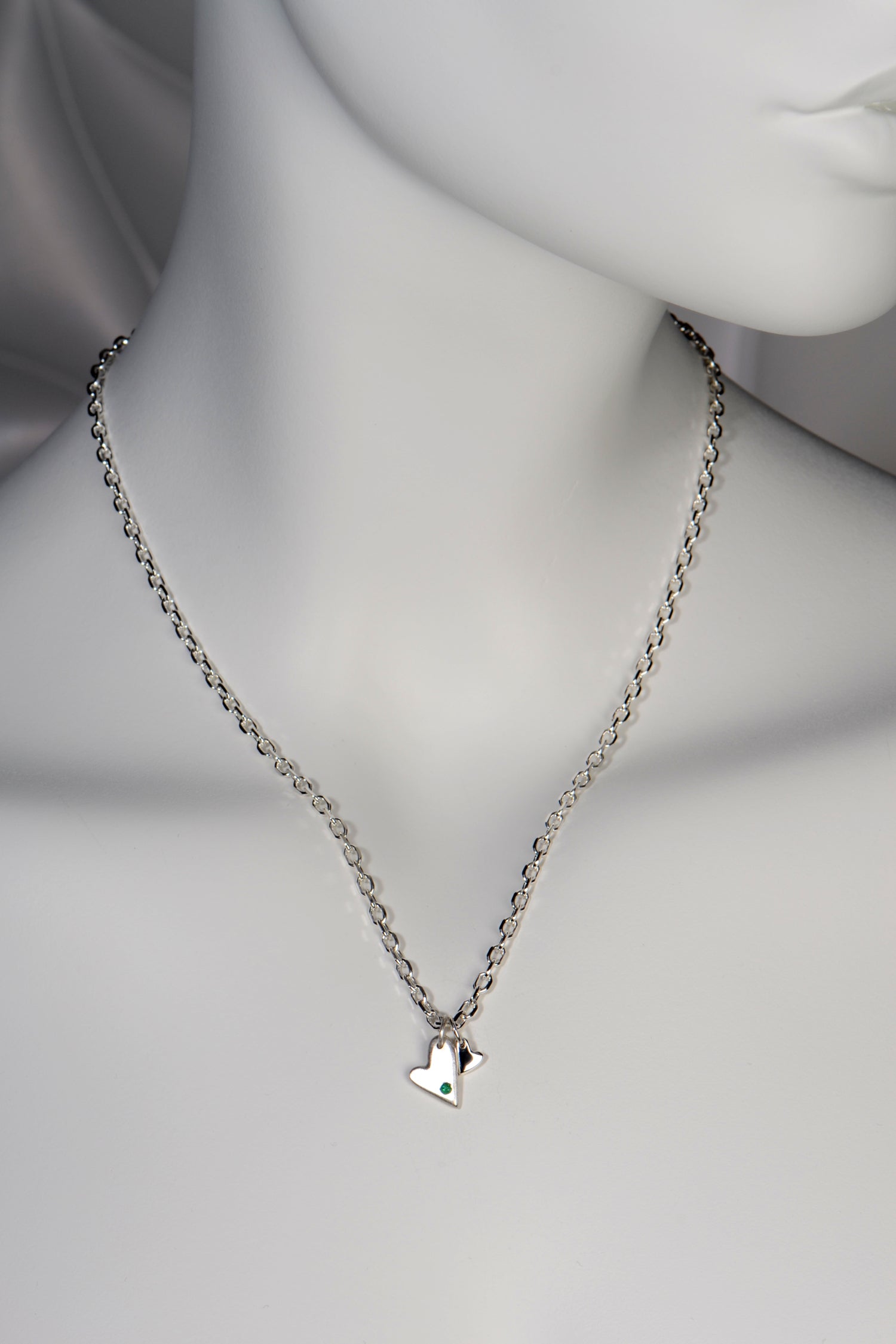 Sterling silver double heart necklace set with emerald displayed on white mannequin to show size and scale 