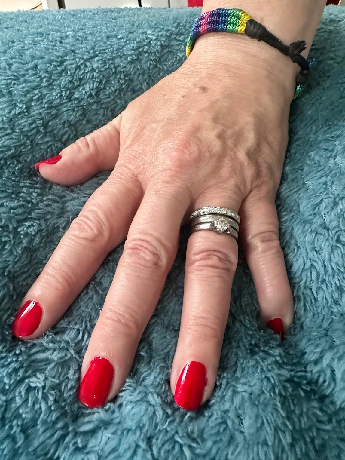 Hand with red nail polish wearing a stack of three platinum rings on a blue textured surface - Christine Sadler eternity ring