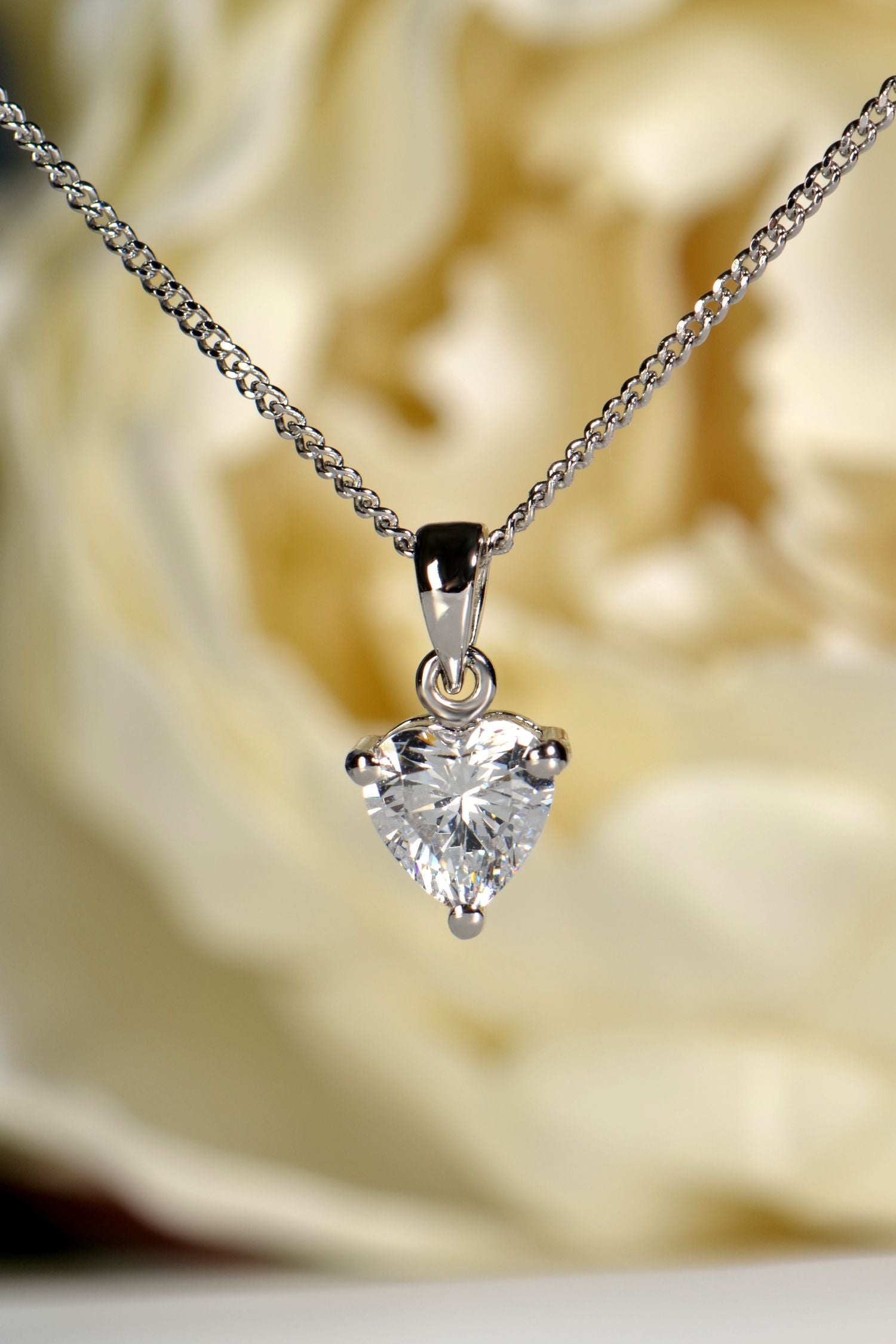 Heart-shaped cubic zirconia pendant on a chain against a blurred floral background