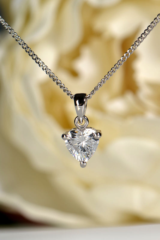 Heart-shaped cubic zirconia pendant on a chain against a blurred floral background