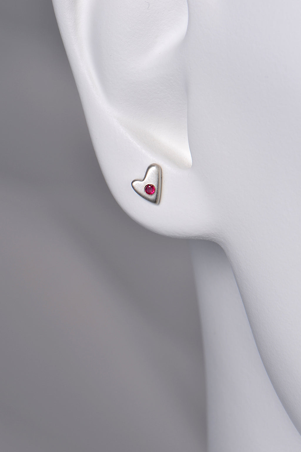 close up of small silver matt heart earrings set with a ruby to show size and scale