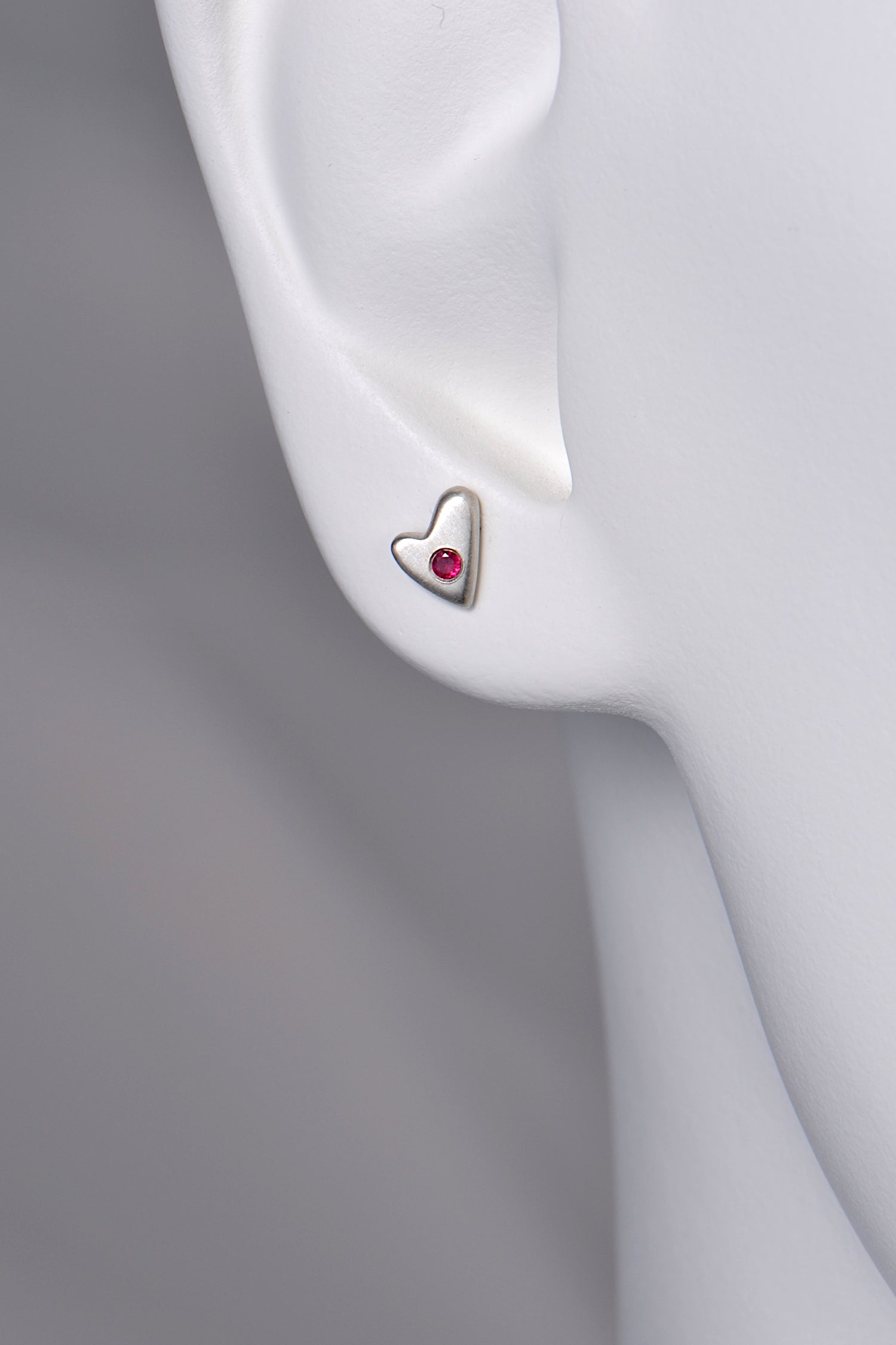 close up of small silver matt heart earrings set with a ruby to show size and scale
