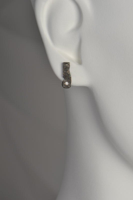 oxidised silver earring in model's ear. It sits on the ear lobe and extends just below it. There is a diamond at the bottom of the rectangular earring.  These designer earrings are by Christine Sadler and are called Hero