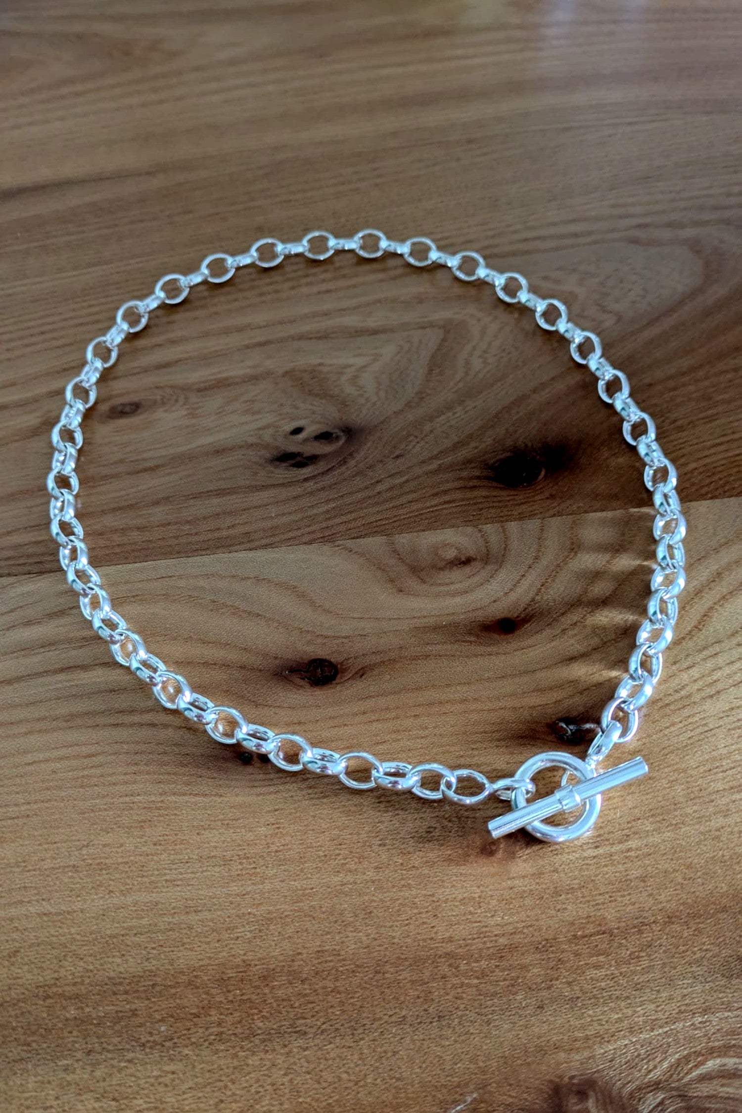 Close-up of sterling silver T-bar necklace on wooden background – durable chain with soldered links
