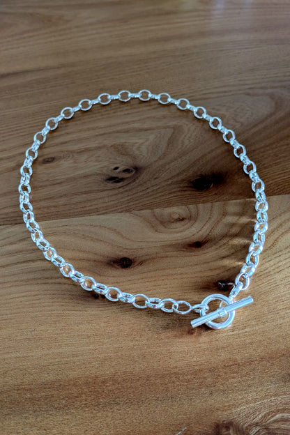 Close-up of sterling silver T-bar necklace on wooden background – durable chain with soldered links