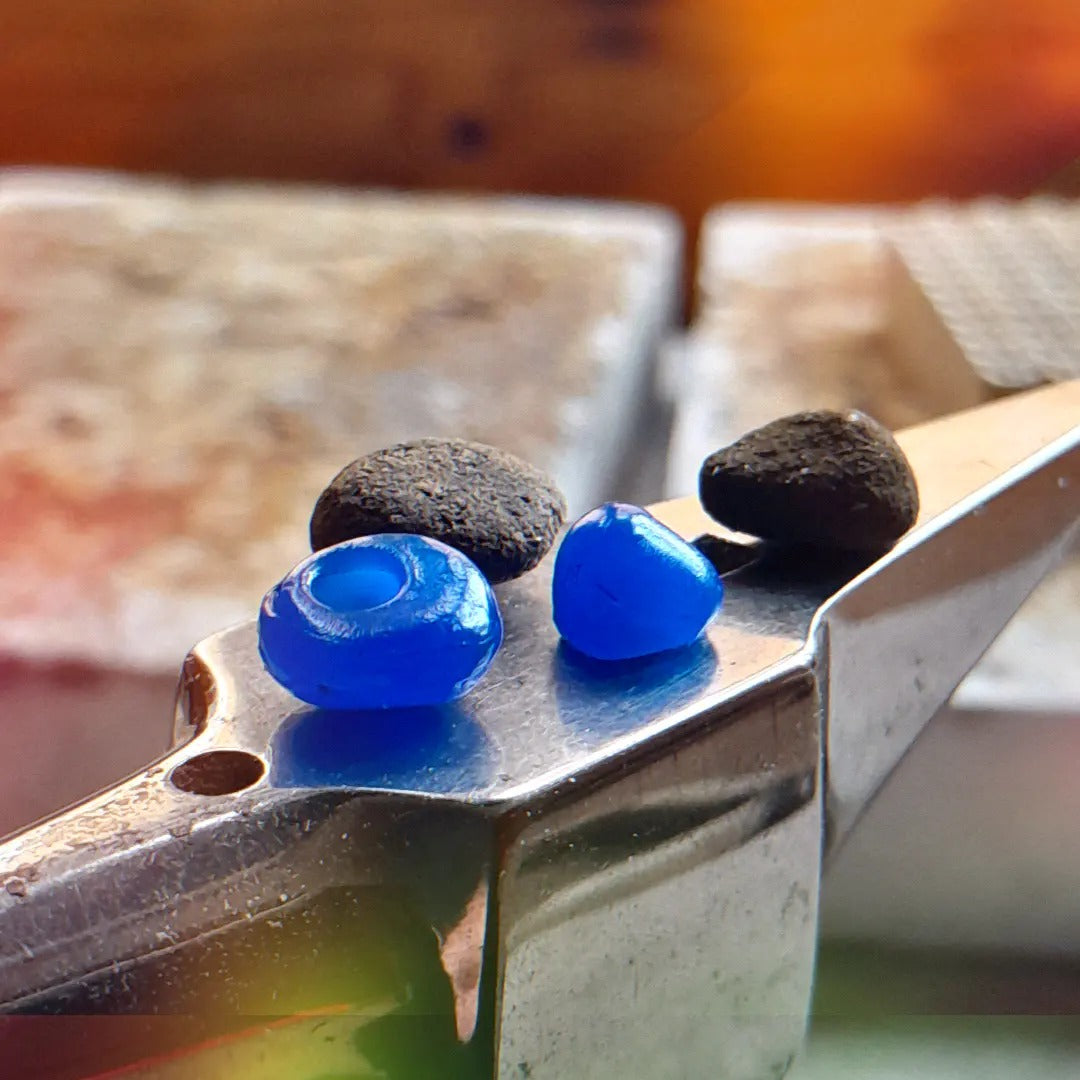 Jewellery workshop showing work in progress for a jewellery commission by Christine Sadler. Two pebbles and two blue wax hand carved settings sit on top of a tiny anvil in Christine's jewellery workshop. 