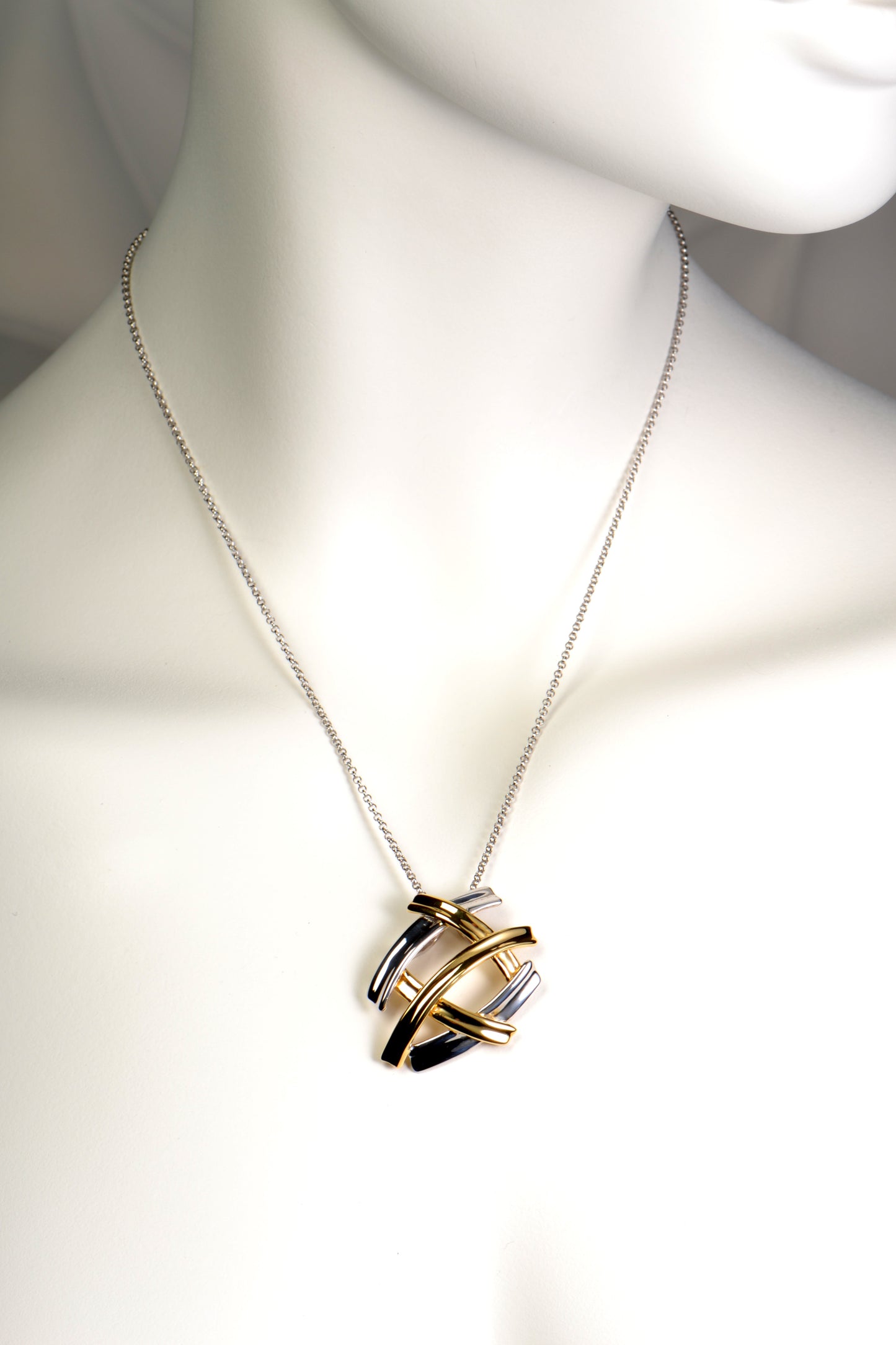 five criss cross bands create a pendant that looks like several large silver and gold kisses. The necklace in silver with gold vermeil.