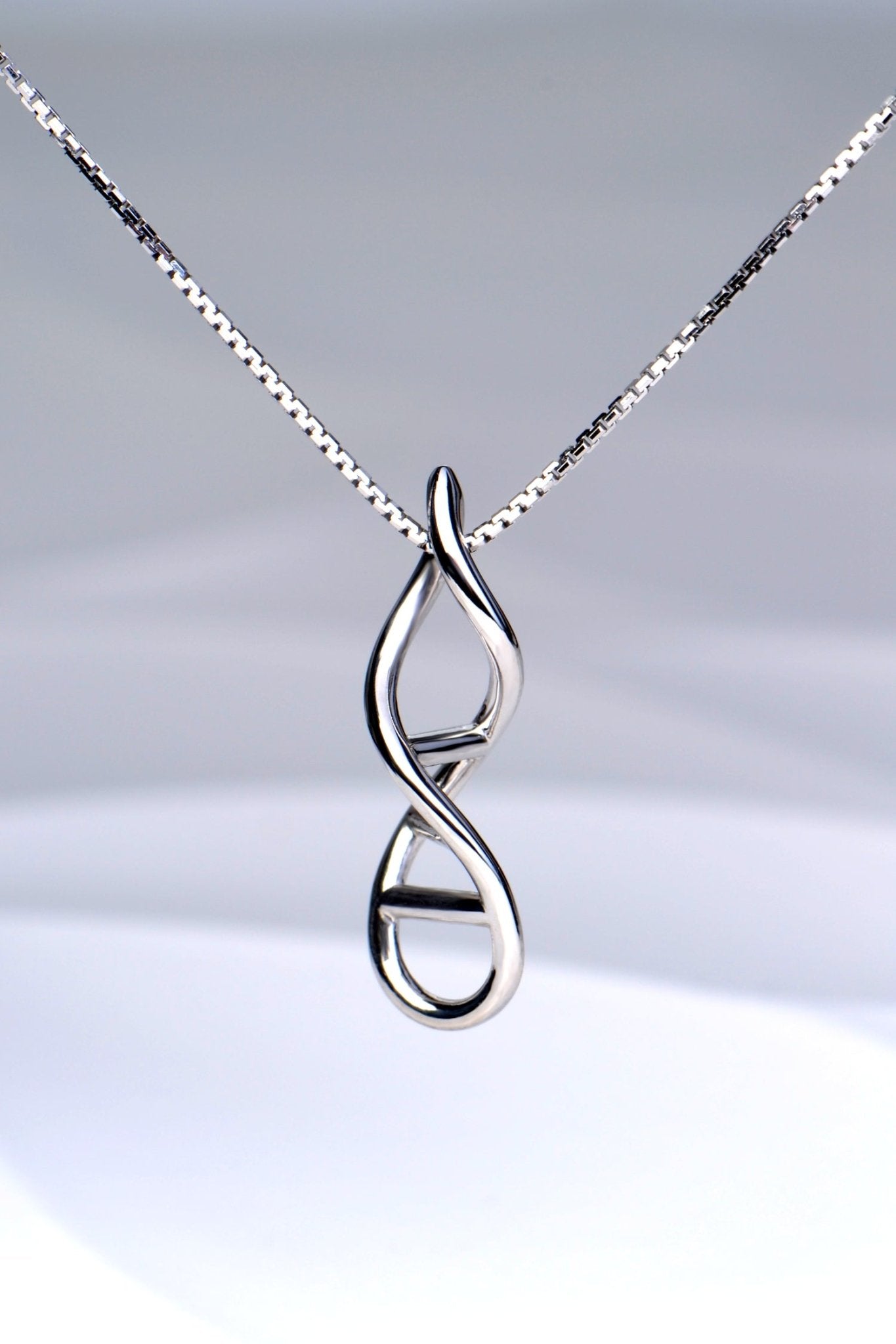 Close-up of sterling silver DNA double helix necklace pendant on a white background - Christine Sadler