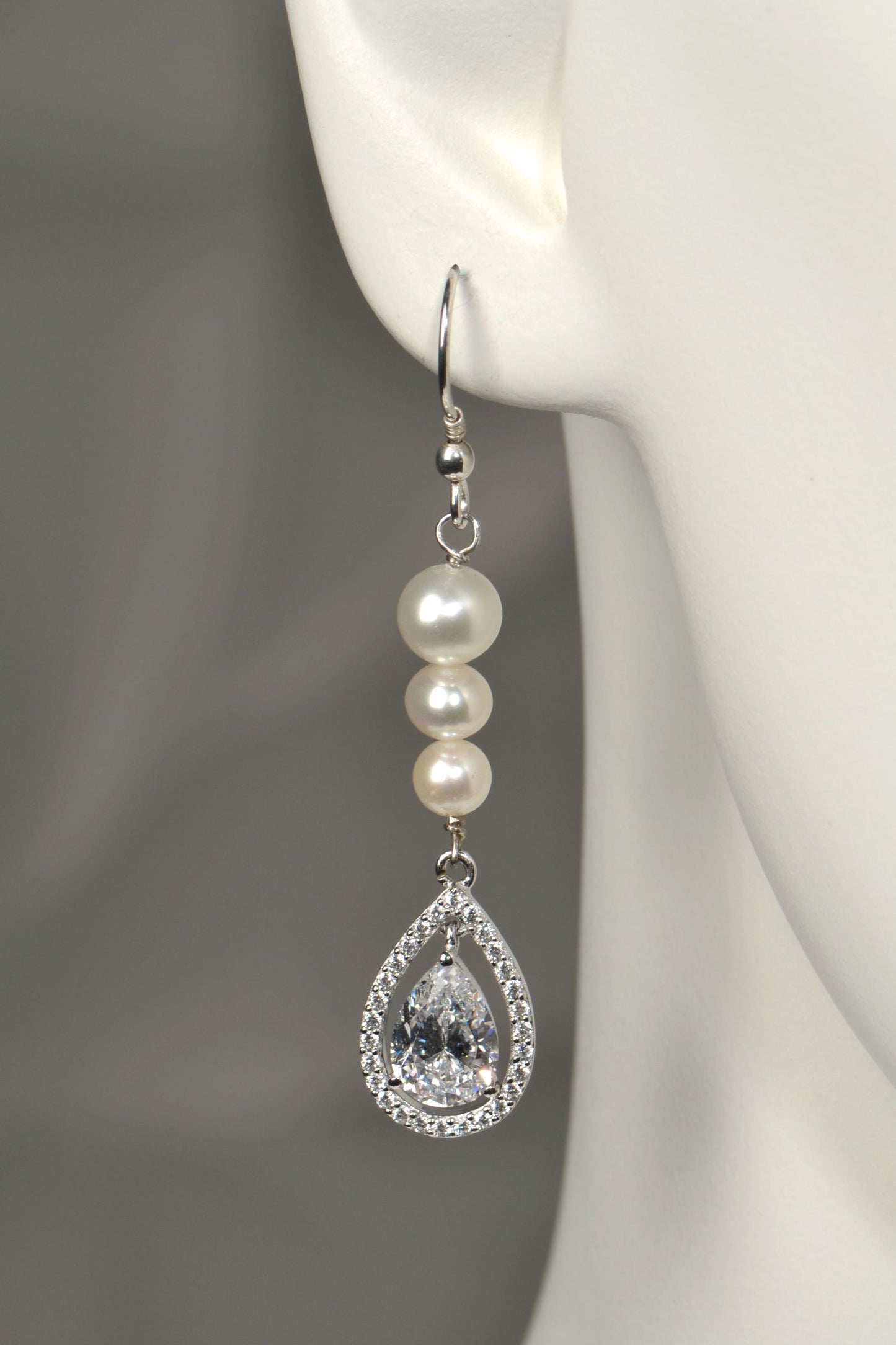 Close-up of graduated pearl drop earring with pear-cut cubic zirconia halo pendant in silver on white mannequin to show the size and scale
