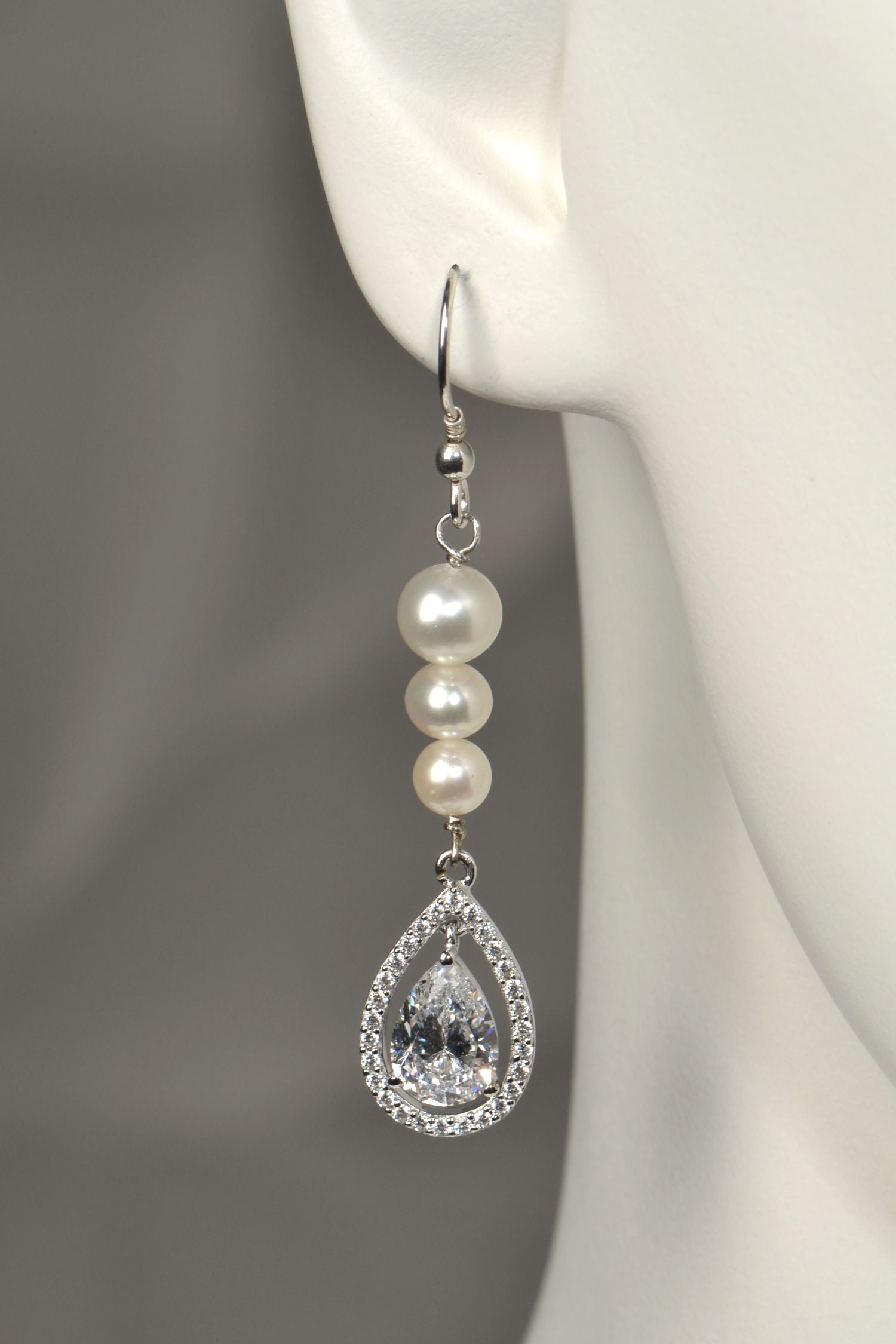 Close-up of graduated pearl drop earring with pear-cut cubic zirconia halo pendant in silver on white mannequin to show the size and scale