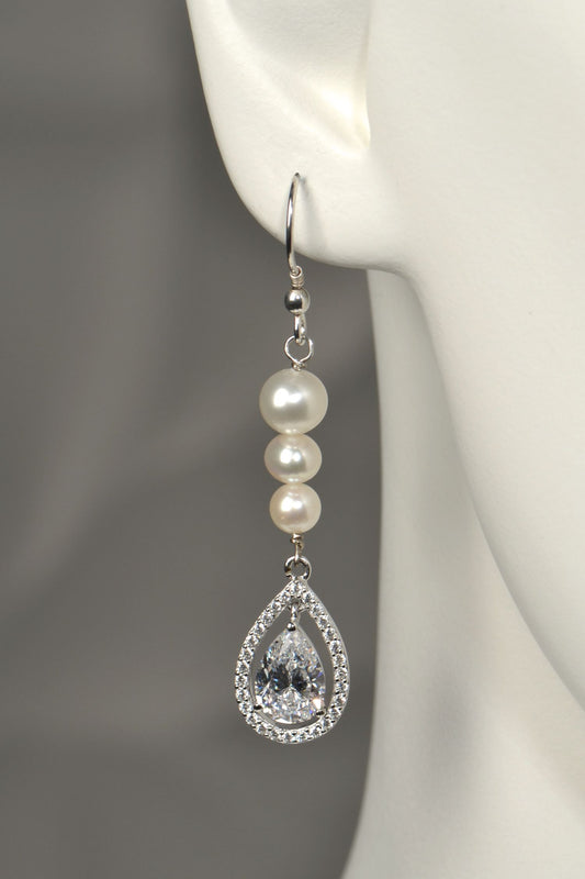 Close-up of graduated pearl drop earring with pear-cut cubic zirconia halo pendant in silver on white mannequin to show the size and scale