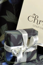 Gift wrapped in Christine Sadler branded thistle and cream rose floral paper with a cream ribbon, placed against a dark background.
