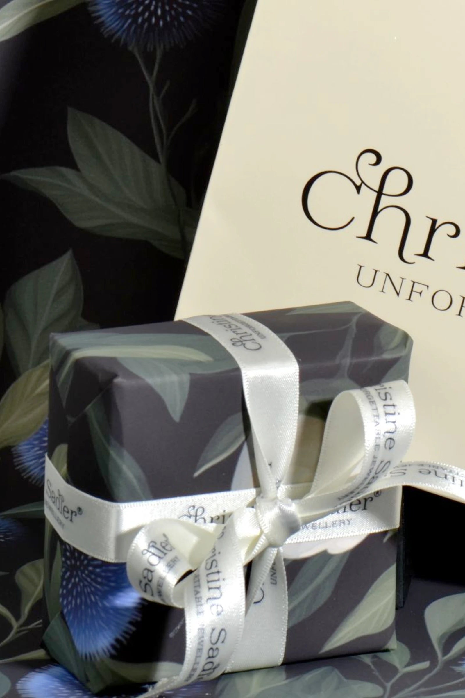 Gift wrapped in Christine Sadler branded thistle and cream rose floral paper with a cream ribbon, placed against a dark background.