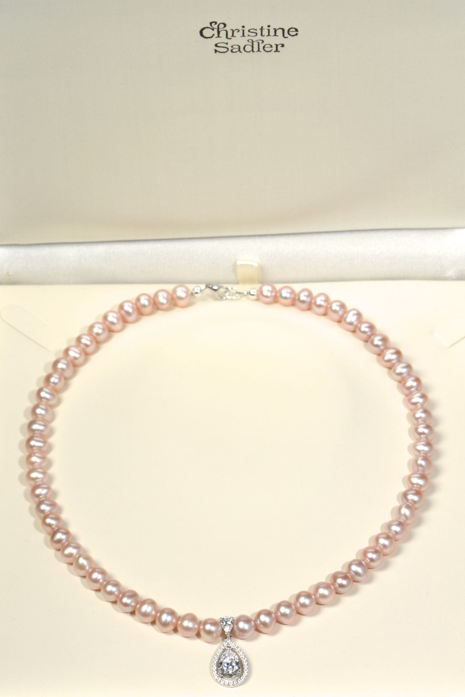 Cultured pink pearl necklace with a diamond pendant on a cream  background, branded 'Christine Sadler'.