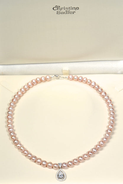 Cultured pink pearl necklace with a diamond pendant on a cream  background, branded 'Christine Sadler'.