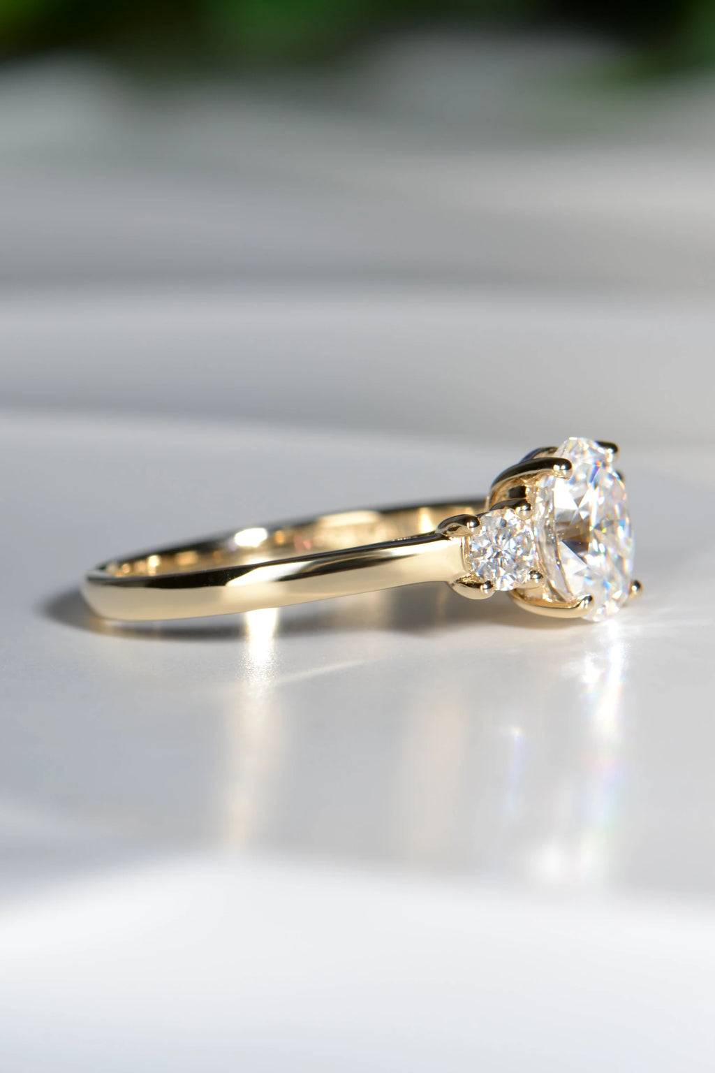 Side profile of a 9ct yellow gold trilogy engagement ring highlighting the straight band design and elevated moissanite gemstone settings.