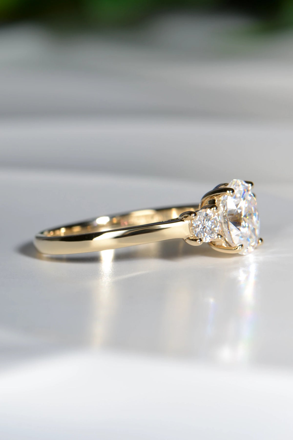 Side profile of a 9ct yellow gold trilogy engagement ring highlighting the straight band design and elevated moissanite gemstone settings.