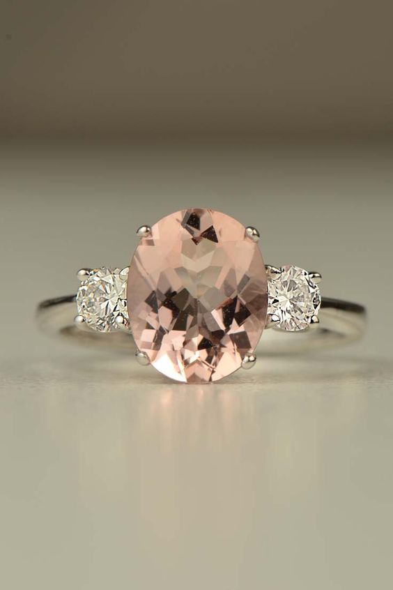 platinum three stone engagement ring set with a large oval morganite with a round white diamond on either side against a grey background - Christine Sadler