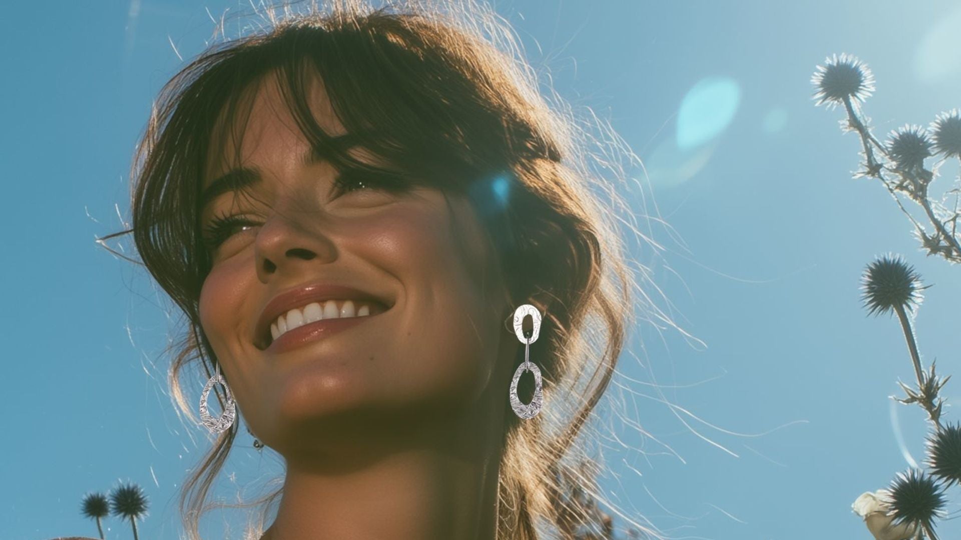 Woman with a bright smile against a clear blue sky wearing large oval drop silver earrings - Natural Beauty design from Christine Sadler Unforgettable Jewellery