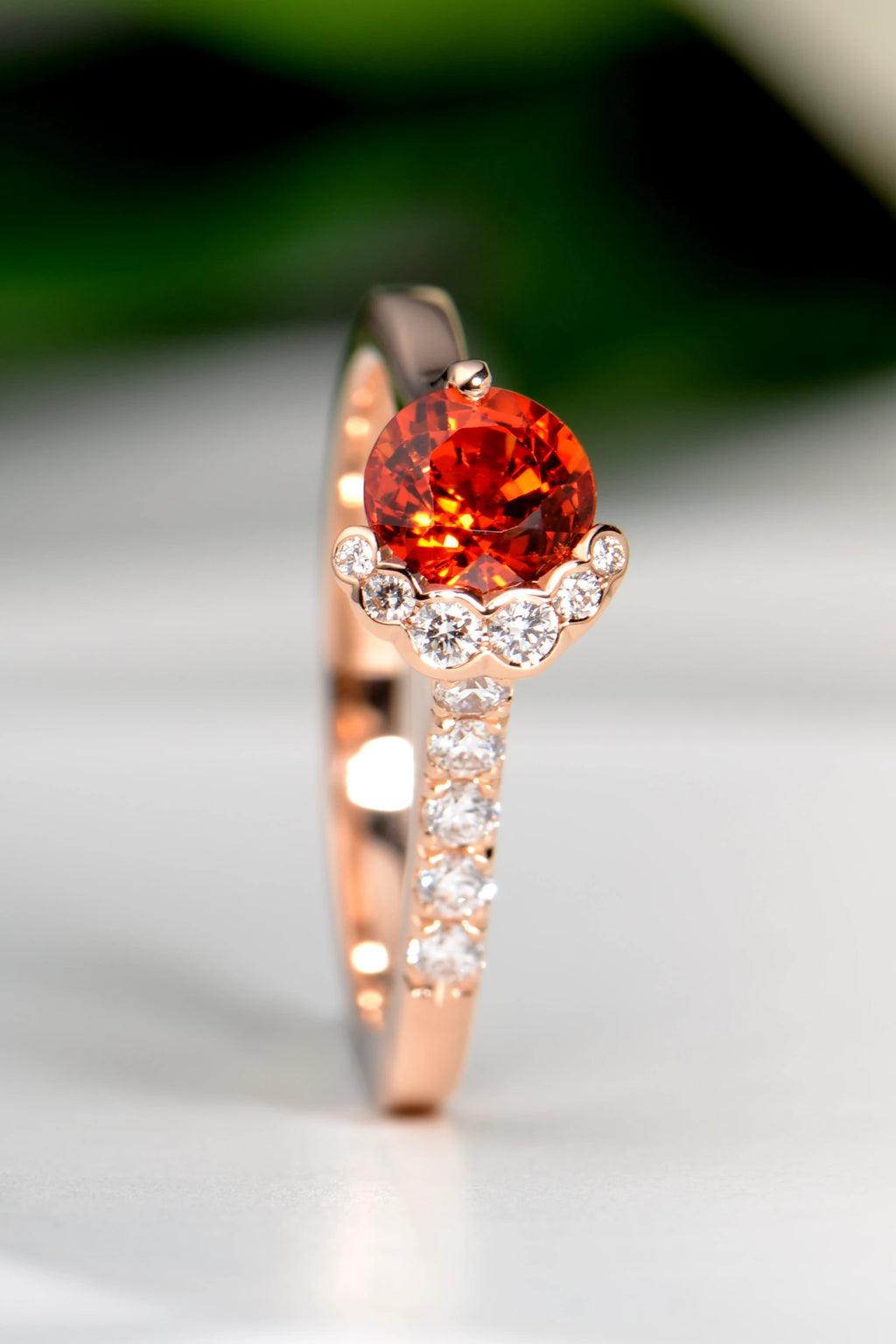 Round orange sapphire above a crescent of diamonds, with a stream of diamonds down the rose gold band.
