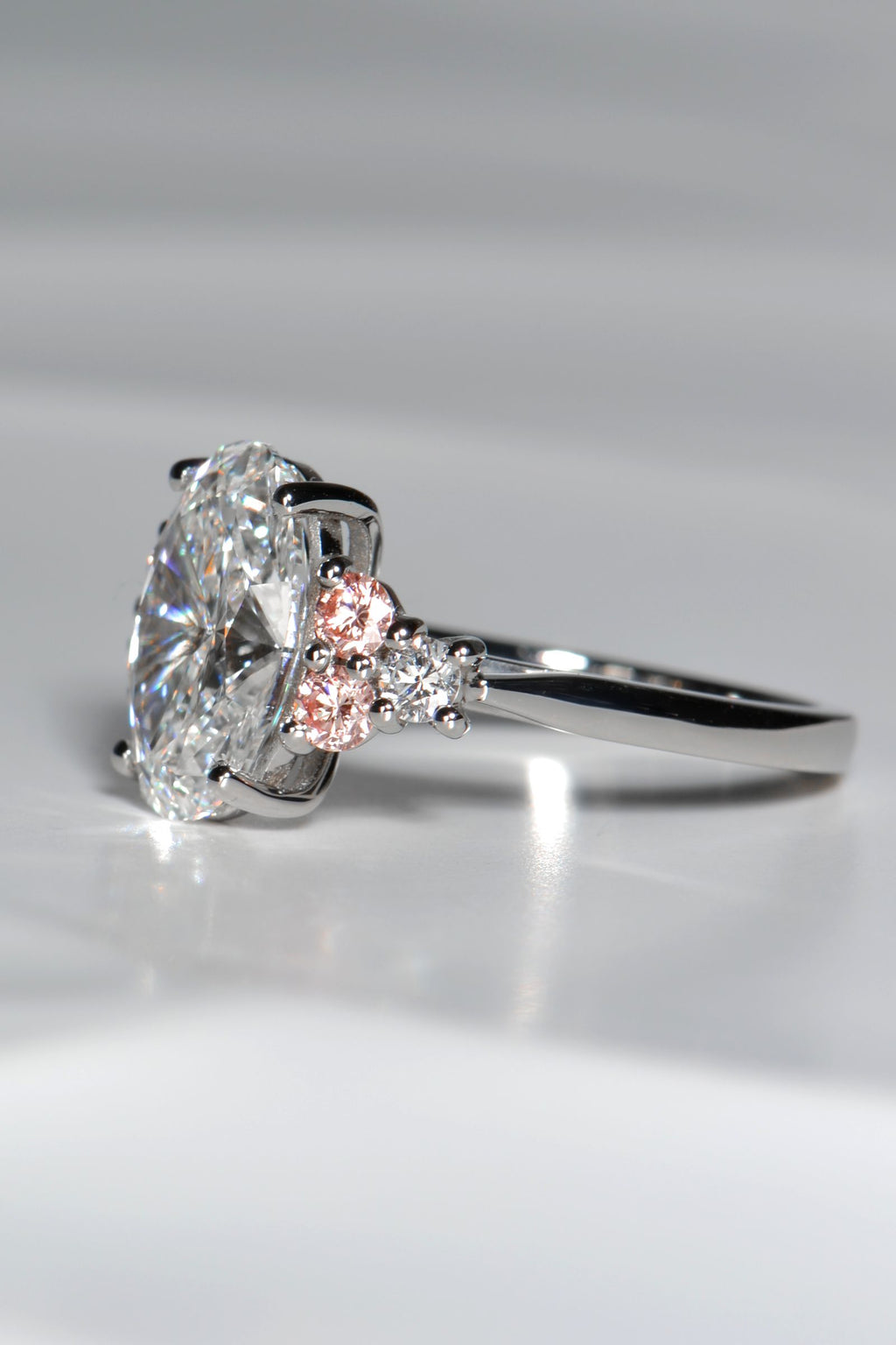 Close-up of Rosé Spark ring showing two pink lab diamonds and one white lab diamond on each side of the central oval stone, forming a white–pink–white sequence.