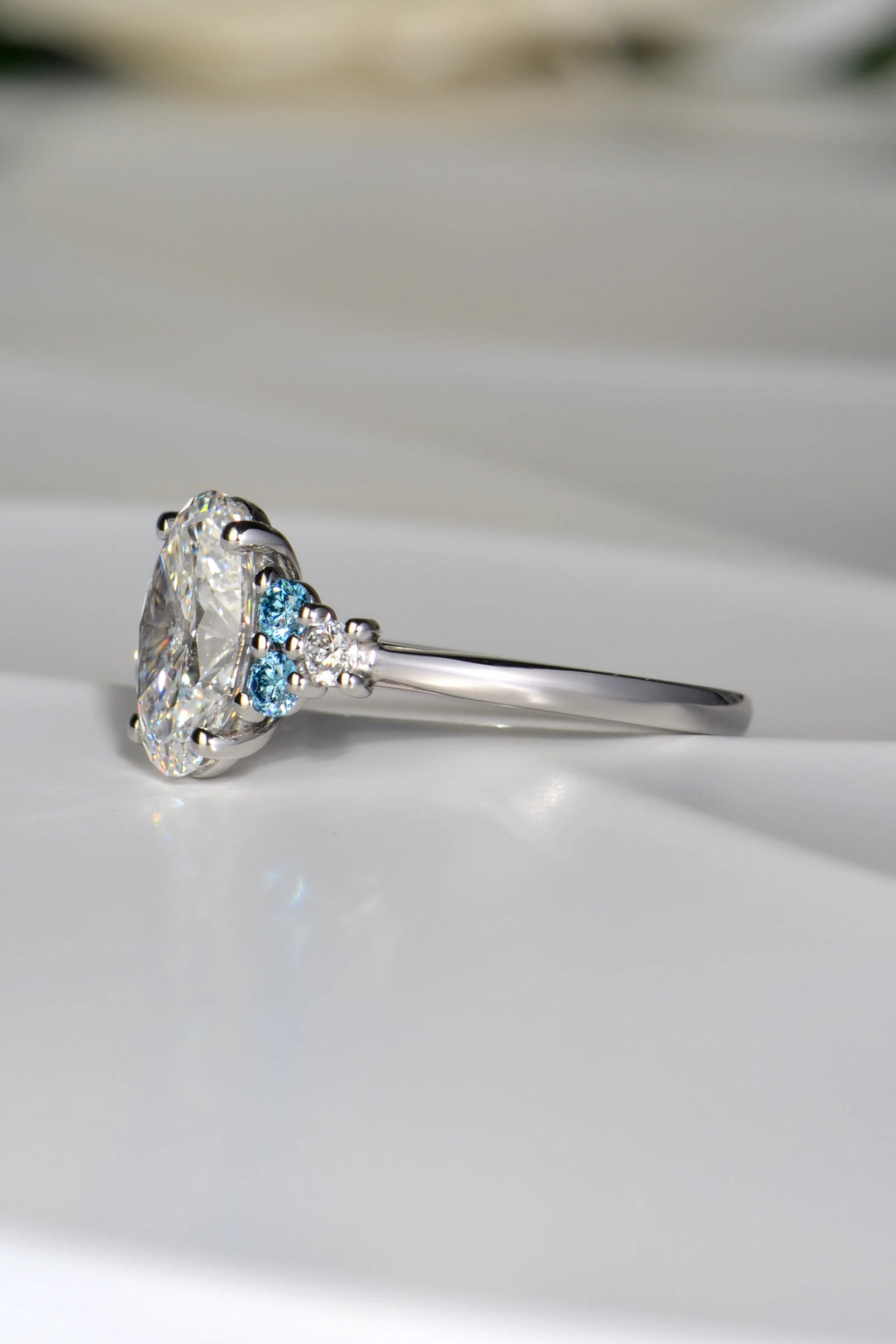 Close-up of the Blue Sky Spark ring showing the round blue lab diamond accents set either side of the oval centre stone and the elegant platinum band