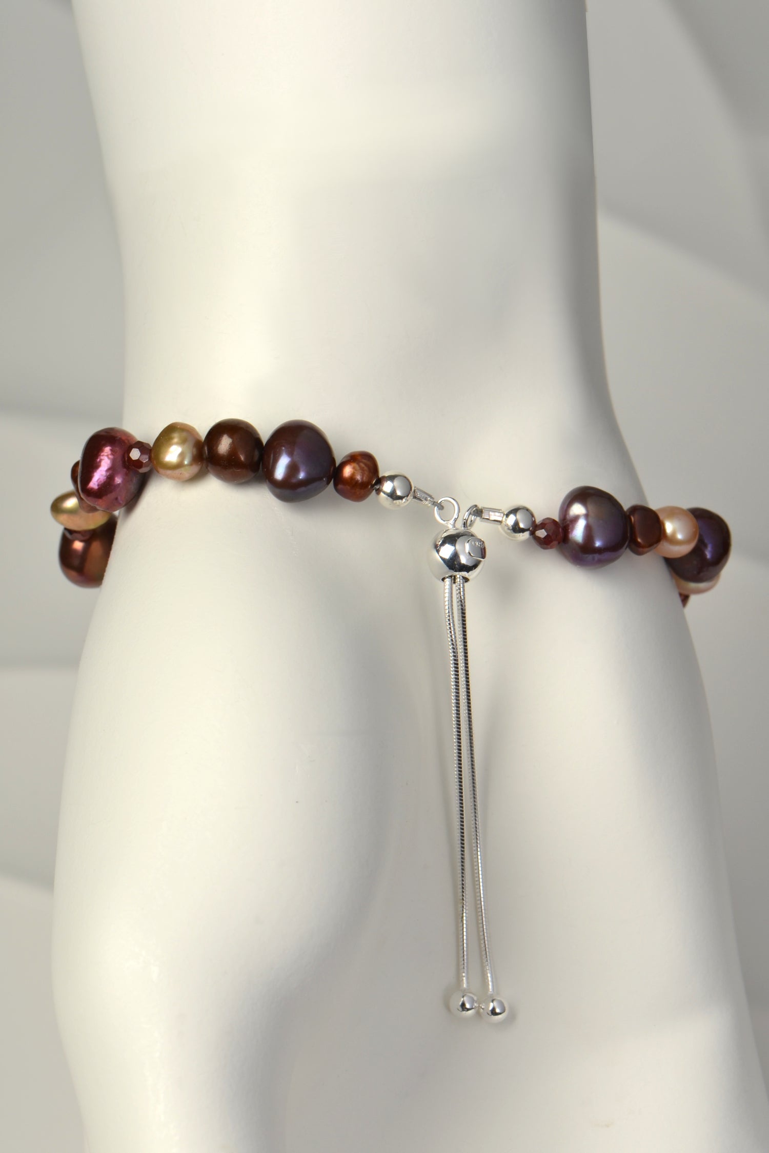 adjustable one of a kind pearl bracelet in pink, brown and golden pearls with garnets and a silver slider clasp. 