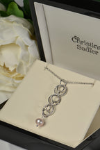 Sterling silver interlocking circle pendant with a pink cultured pearl at the bottom in a Christine Sadler branded gift box with peony rose in the background