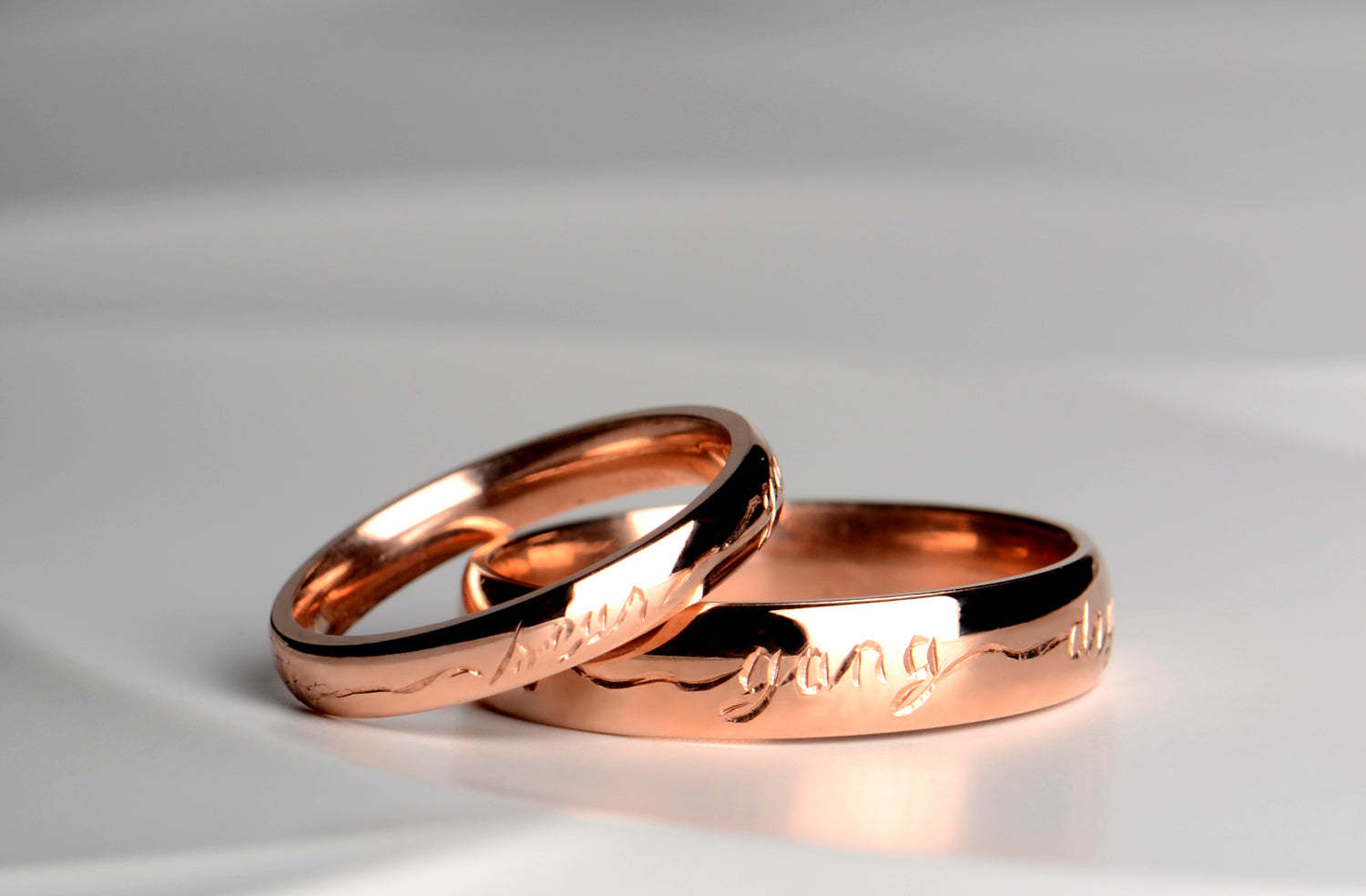 Personalised wedding rings handmade in the UK by british jewellery designer Christine Sadler. The photograph shows a matching pair of his and hers wedding rings in rose gold hand engraved with a scottish poetry phrase by Robert Burns.