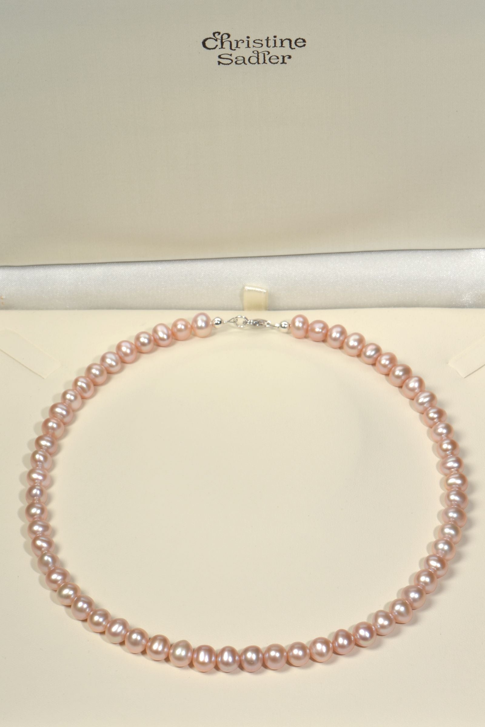 Pink cultured pearl necklace on a cream presentation box with 'Christine Sadler' branding.