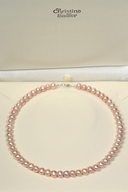Pink cultured pearl necklace on a cream presentation box with 'Christine Sadler' branding.