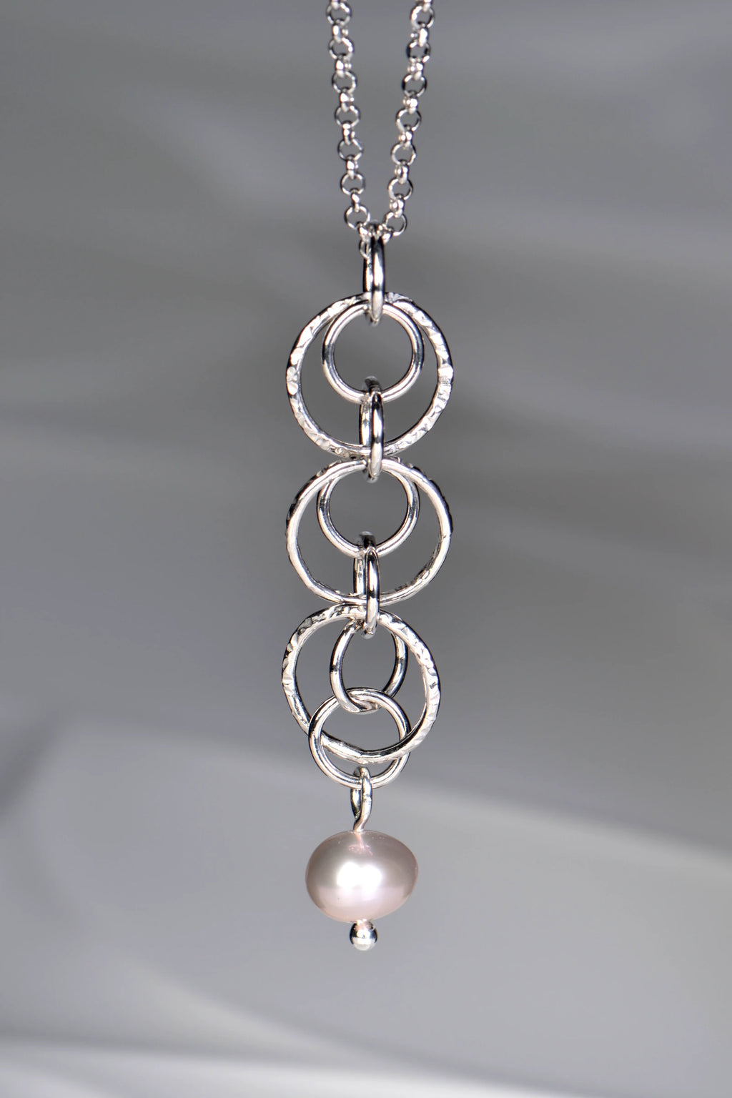 Sterling silver pendant with interlocking rings and a cultured pink pearl at the bottom on a 45cm long rolo silver chain on a gray background