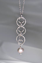 Sterling silver pendant with interlocking rings and a cultured pink pearl at the bottom on a 45cm long rolo silver chain on a gray background