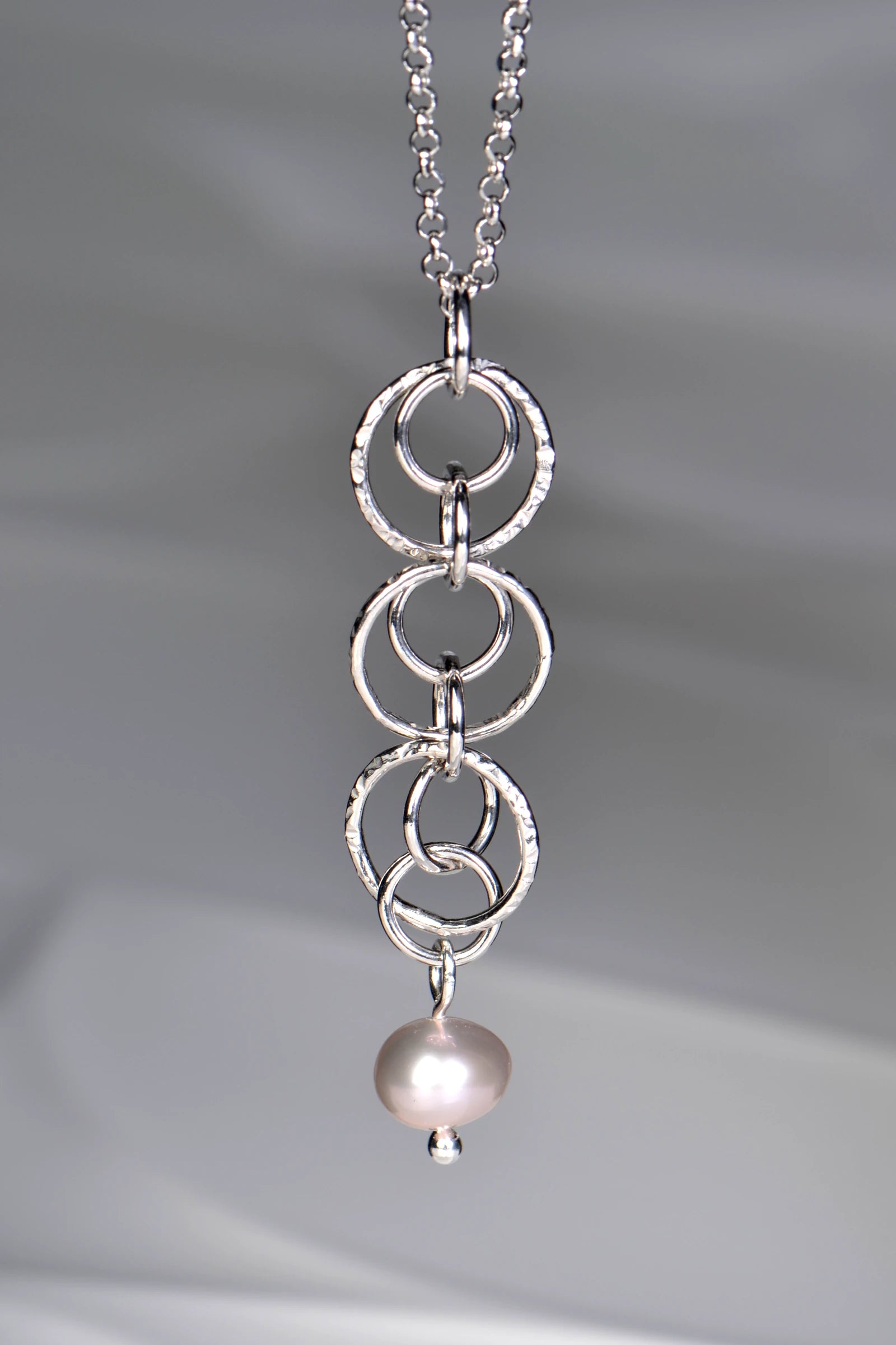 Sterling silver pendant with interlocking rings and a cultured pink pearl at the bottom on a 45cm long rolo silver chain on a gray background