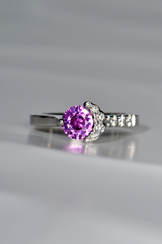 incredible pink sapphire round gemstone surrounded on one side by a crescent of brilliant cut white diamonds that flow down into more diamonds on one side of the ring, made in platinum, one of a kind. 