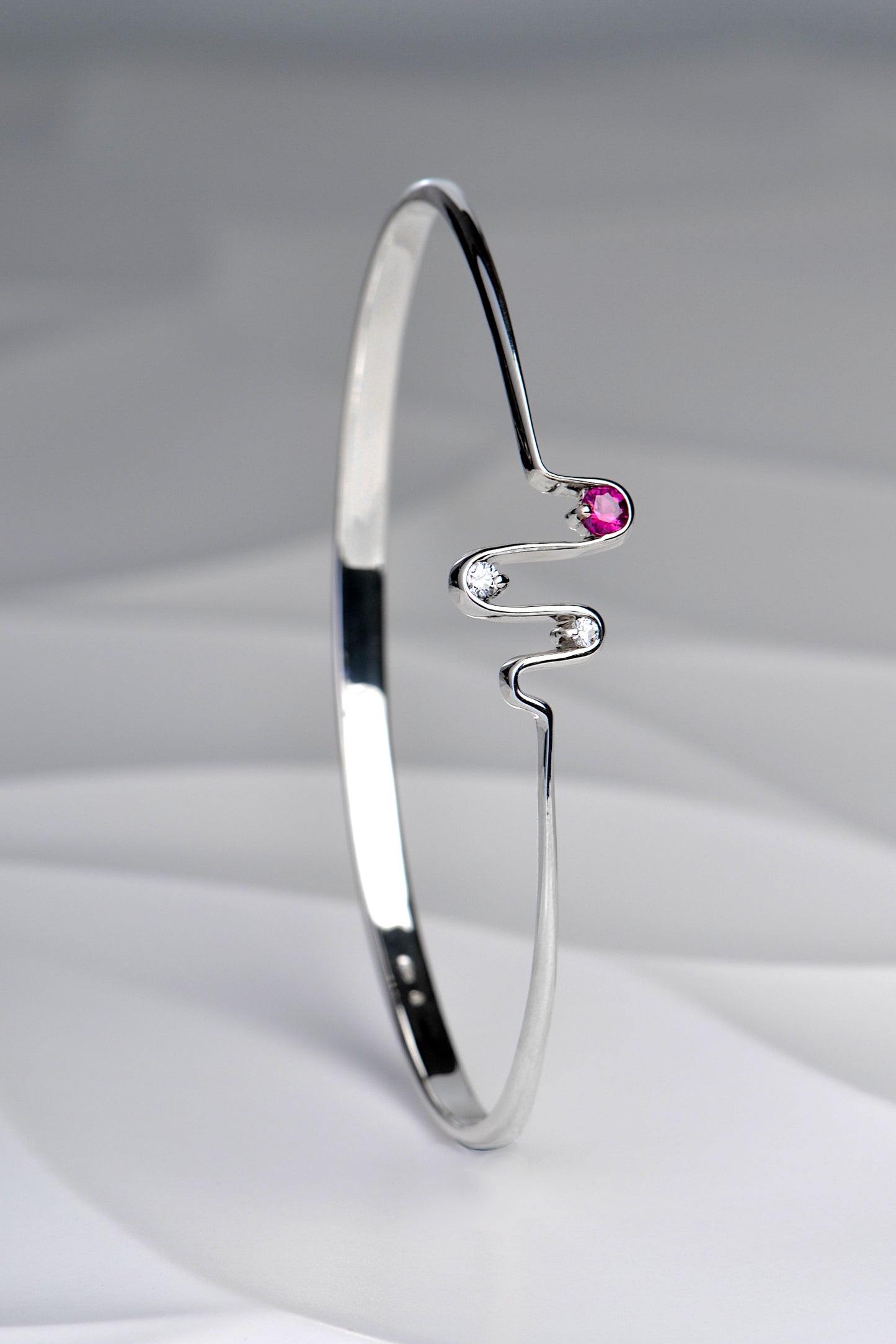 silver heartbeat wave bangle set with two diamonds and a pink sapphire