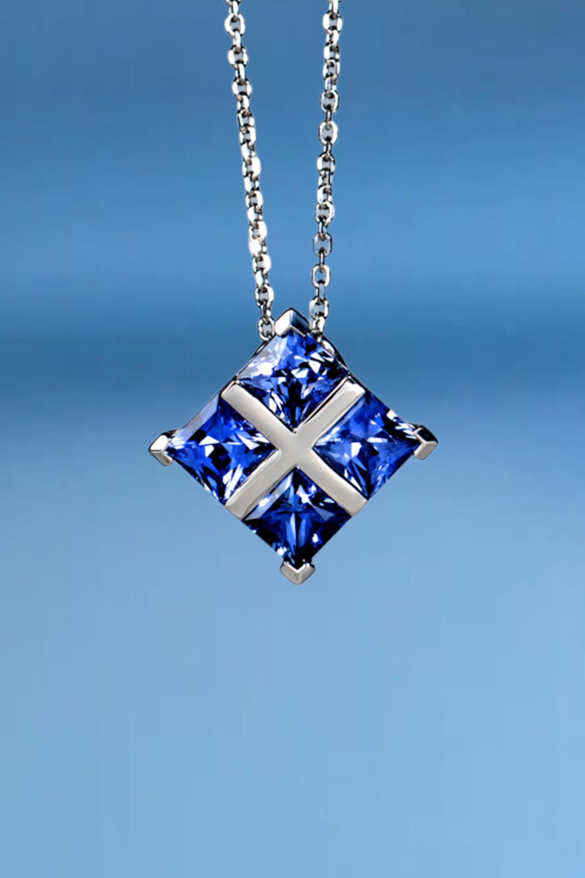 Luxury tartan-patterned platinum pendant necklace featuring four princess-cut blue sapphires.