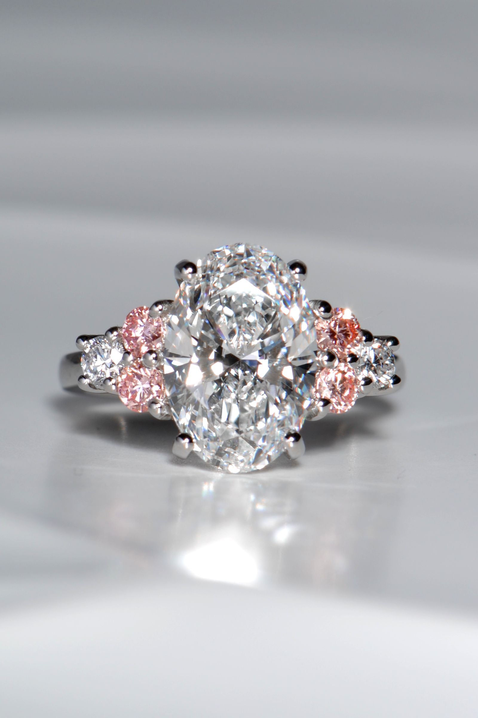 Rosé Spark platinum 950 oval lab diamond ring viewed from above, featuring a 3ct central white lab diamond and six brilliant-cut side stones with pink lab diamond accents.