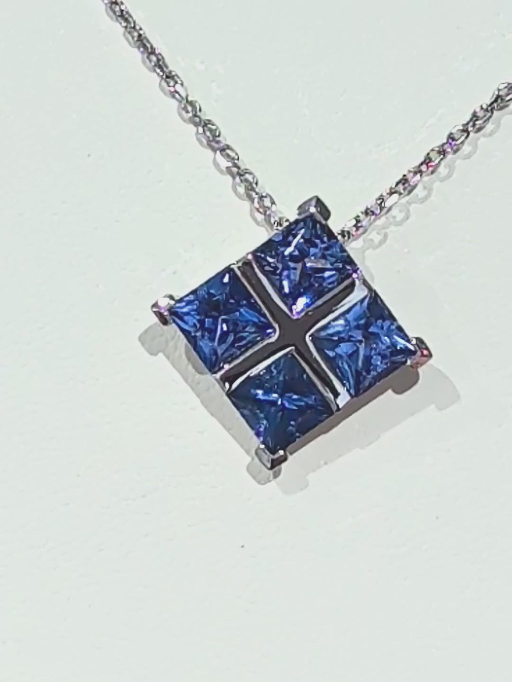 A close-up video tracking a luxury platinum chain to a Tartan pendant, showing the brilliant sparkle and deep blue color of four princess-cut sapphires catching the light.