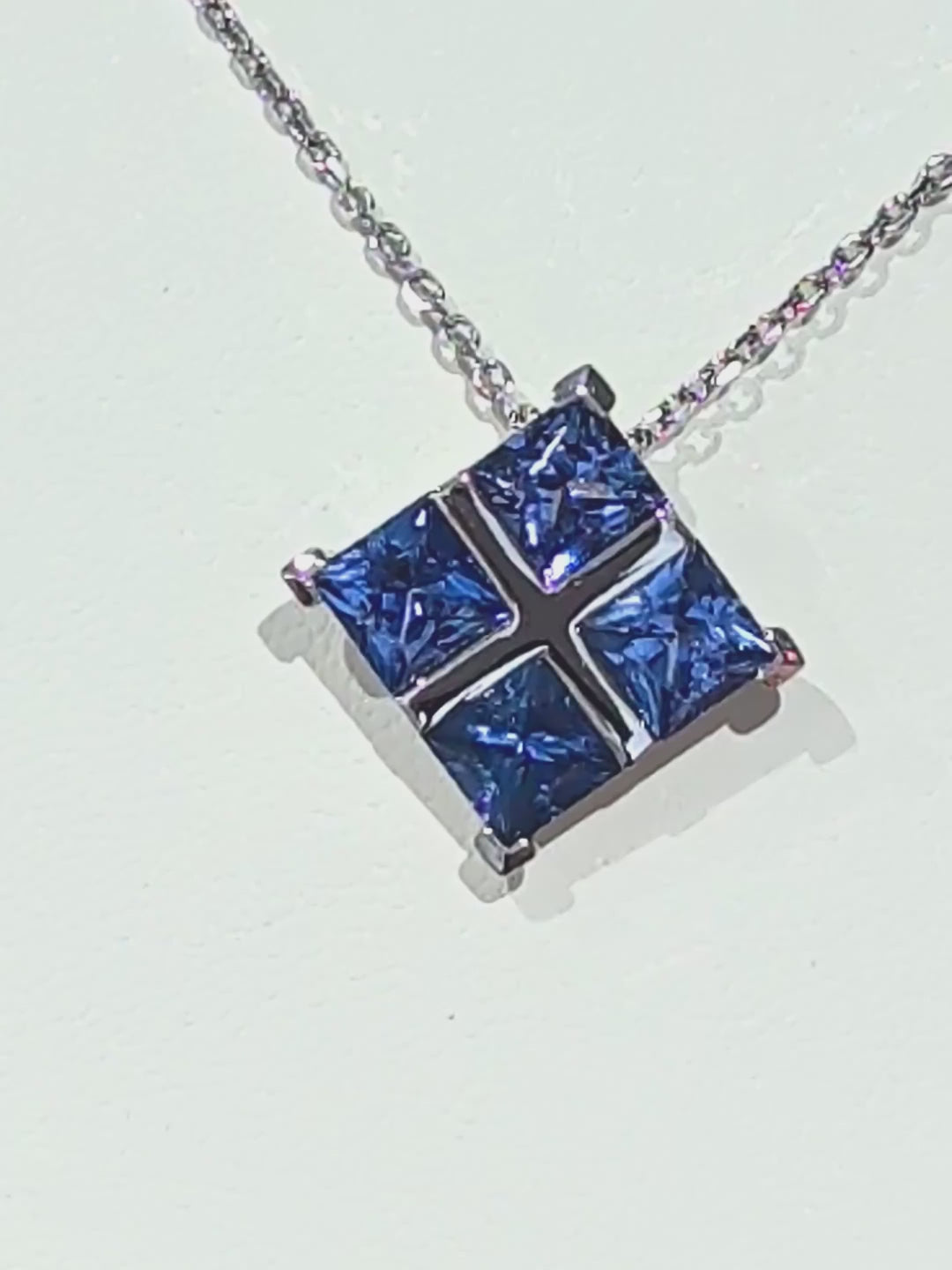 A close-up video tracking a luxury platinum chain to a Tartan pendant, showing the brilliant sparkle and deep blue color of four princess-cut sapphires catching the light.