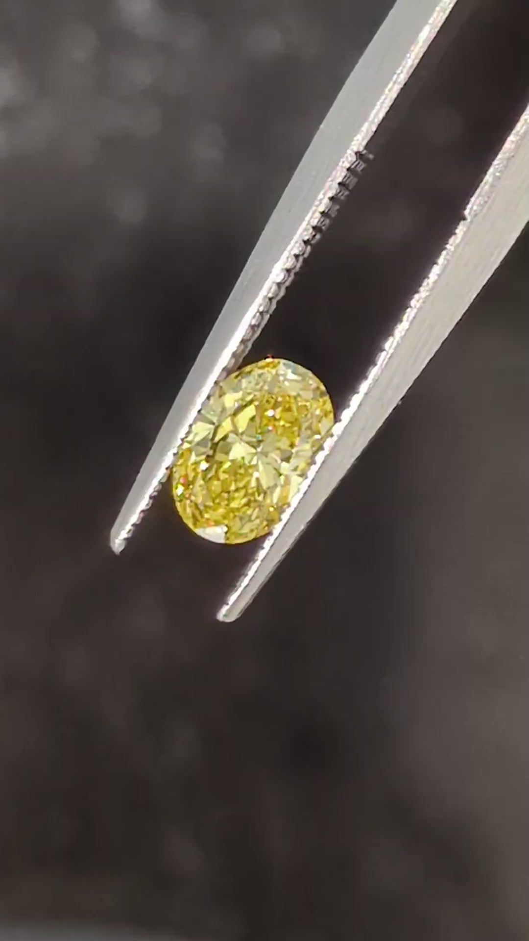 oval cut yellow lab diamond held in twezzers with a black and brown stone background - jeweller Christine Sadler