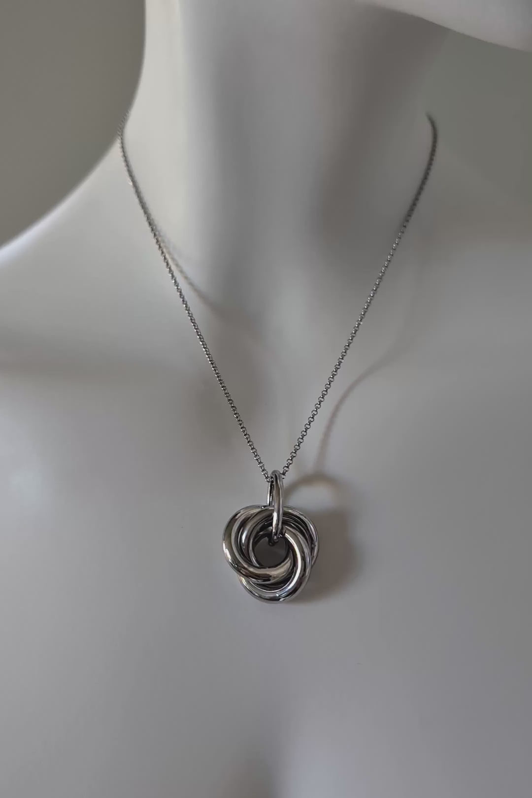 A large silver intolocking knot pendant on a siler chain shown from different angles.