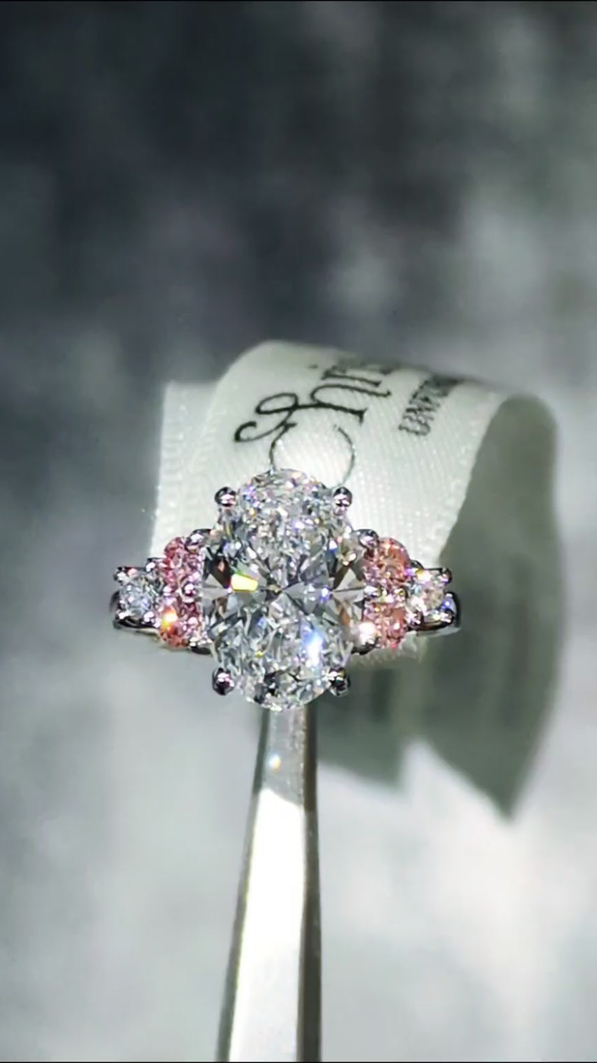 Rosé Spark platinum 950 oval lab diamond ring moving to reveal maximum sparkle from the central 3ct white lab diamond and six side stones with pink accents.