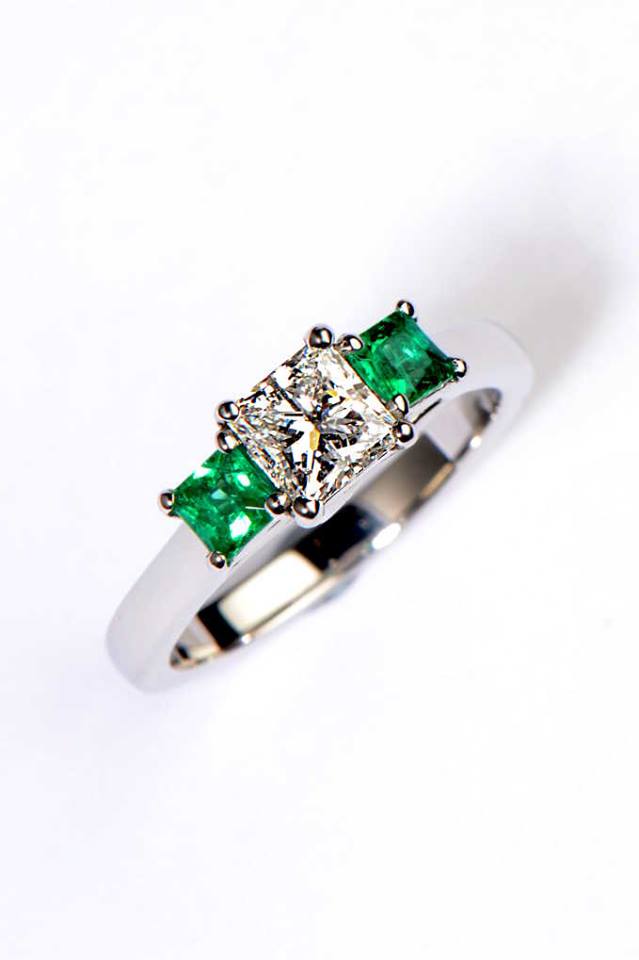 Three stone platinum engagement ring with a princess cut diamond in the middle and an emerald on either side - Christine Sadler