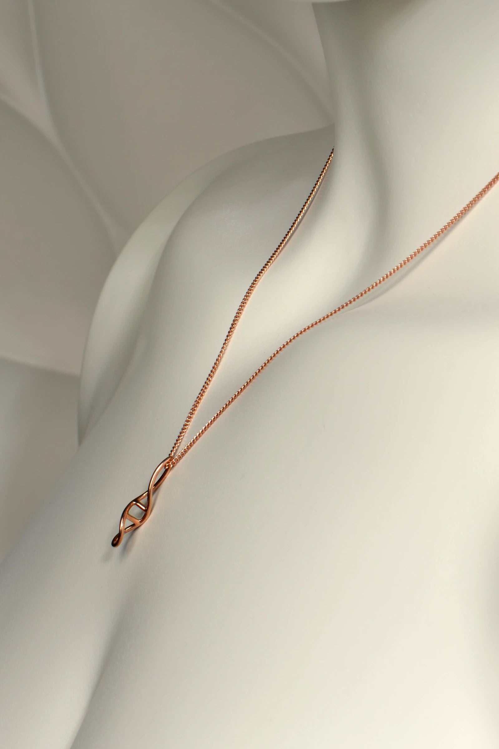 handcrafted 9ct rose gold necklace in double helix shape on a mannequin with a soft, neutral background from jewellery designer Christine Sadler