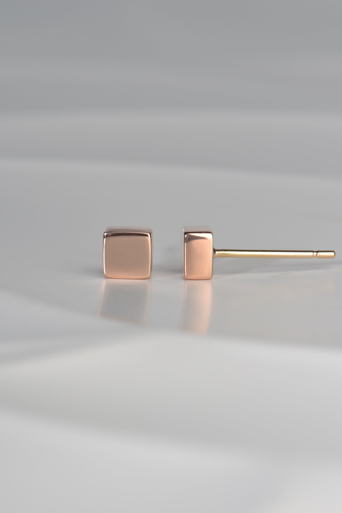 side view of rose gold 5mm square earrings showing that they are deep and substantial and look like minature blocks of stone.